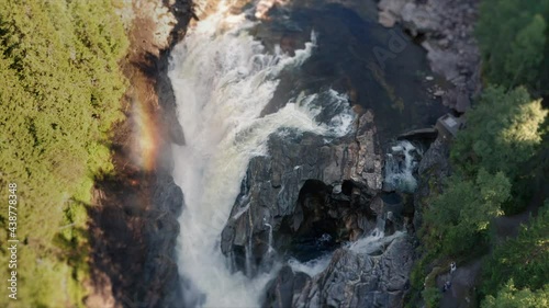 A forward-moving shot of the wild river at the Formofossen waterfall. Rainbow is hanging above the waterfall as the sunlight is reflected in the millions of water droplets made by the falling water. photo