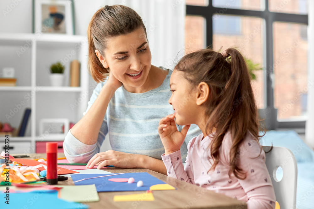 family, art and craft concept - mother spending time with her little daughter with glue making applique of color paper at home