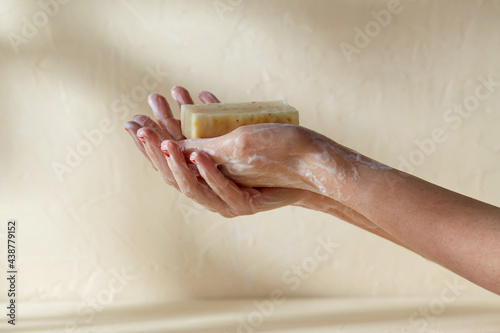 natural cosmetics, hygiene and beauty concept - foamy hands holding bar of craft soap on beige background photo