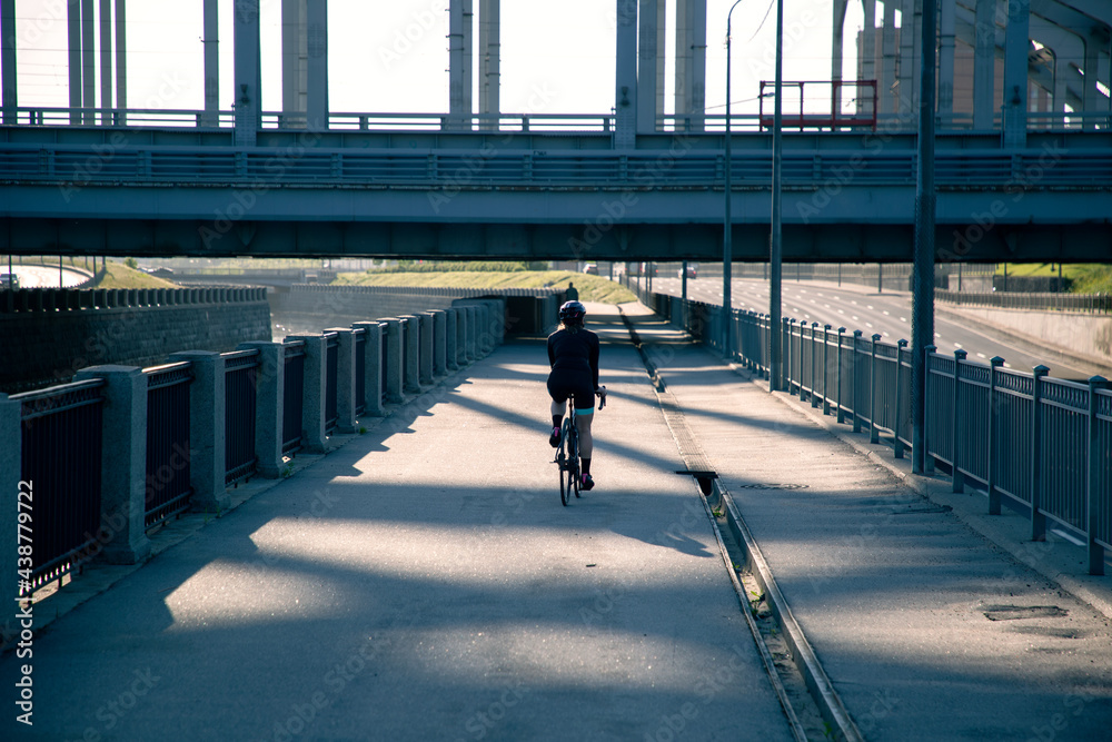 Rear view of a female cyclist in the morning illuminated by the sun. Morning workout on a bike.