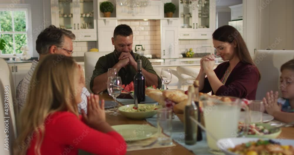 Caucasian parents, children and grandfather sitting at table for family meal saying prayers