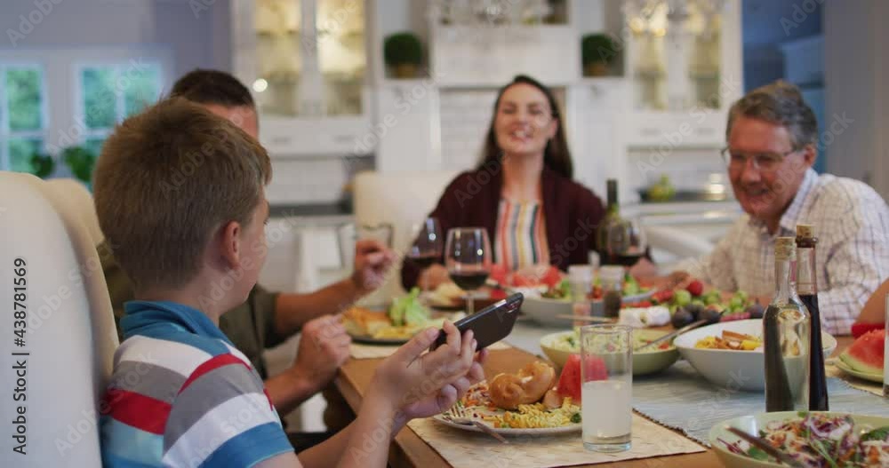 Happy caucasian grandson taking selfie with parents and grandfather at table during family meal Happy caucasian grandson taking selfie with parents and grandfather at table during family meal