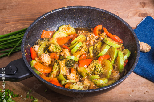 Vegetarian dish of broccoli, zucchini, onions and tomato in a skillet. Vegetables are stewed in a wok. Frying pan with vegetables on the table, top view
