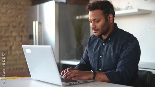 Smart and clever indian male freelancer using laptop computer for work on the distance, focused mixed-race eastern guy is typing, texting, messaging online, working at new project from home