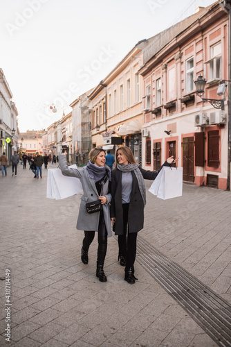 Two beautiful fashion Caucasian women walk down the street smiling and carrying bags with purchased clothes. Autumn shopping in the city © Dragica