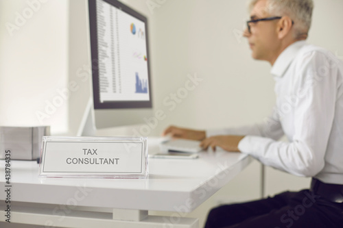 Senior tax consultant working at computer. Male Tax Accountant consultant Doing Sales Invoice Accounting. Tax consultant in white shirt and glasses