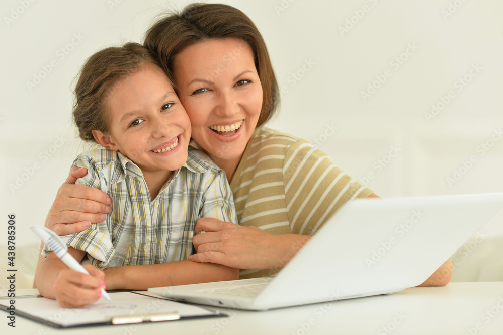 Cute girl and mother using laptop at home at desk Cute girl and mother using laptop at home at desk