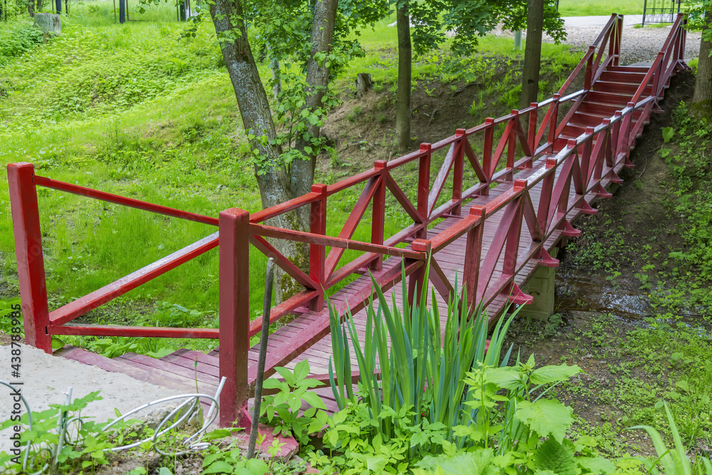 A small bridge made of wooden boards with handrails across a narrow stream in a city park A small bridge made of wooden boards with handrails across a narrow stream in a city park