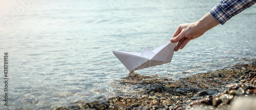 Foto Woman's hand is launching a white paper boat into the clear water of a large lak