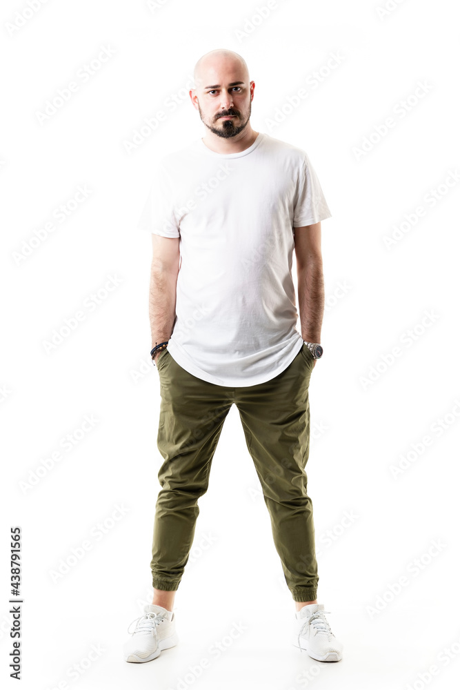 Confident trendy stylish young bald bearded man looking at camera with hands in pockets. Full body length isolated on white background Confident trendy stylish young bald bearded man looking at camera with hands in pockets. Full body length isolated on white background