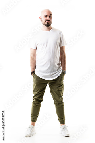 Distrustful expression of young bald man looking at camera with raised eyebrow. Full body length isolated on white background