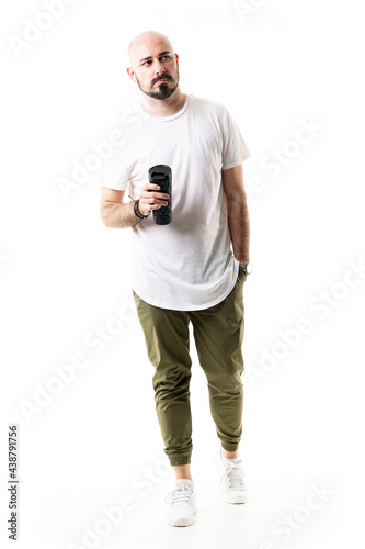 Handsome stylish bald young man walking holding water or coffee container. Full body length isolated on white background
