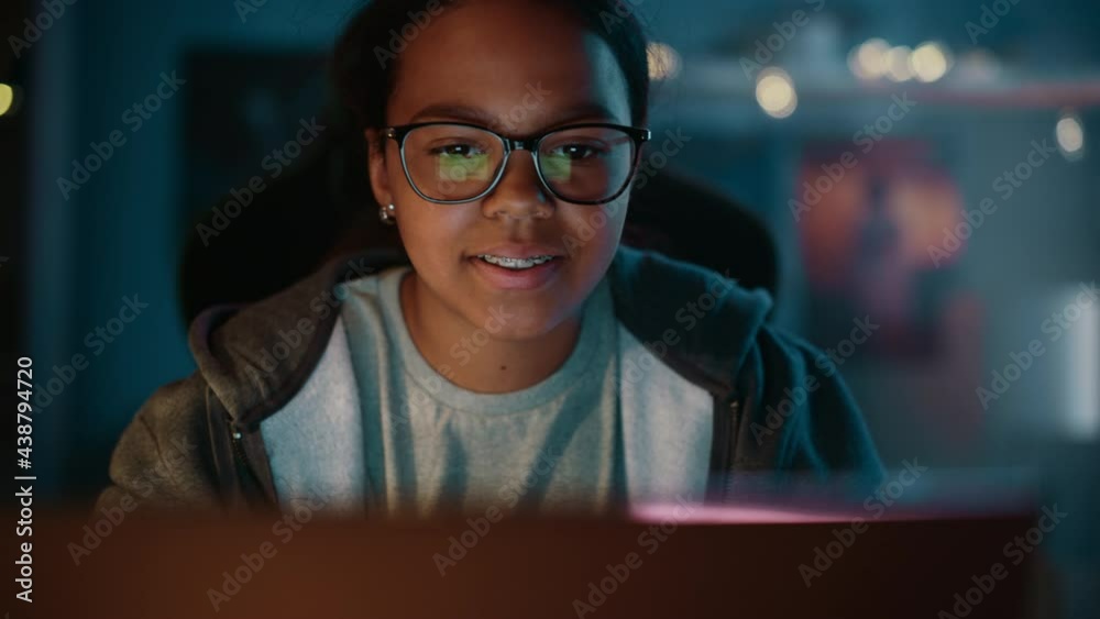 Young Teenage Multiethnic Black Girl Using Laptop Computer in a Dark Cozy Room at Home. She's Browsing Educational Research Online. Studying Science School Homework Concept. Young Teenage Multiethnic Black Girl Using Laptop Computer in a Dark Cozy Room at Home. She's Browsing Educational Research Online. Studying Science School Homework Concept.
