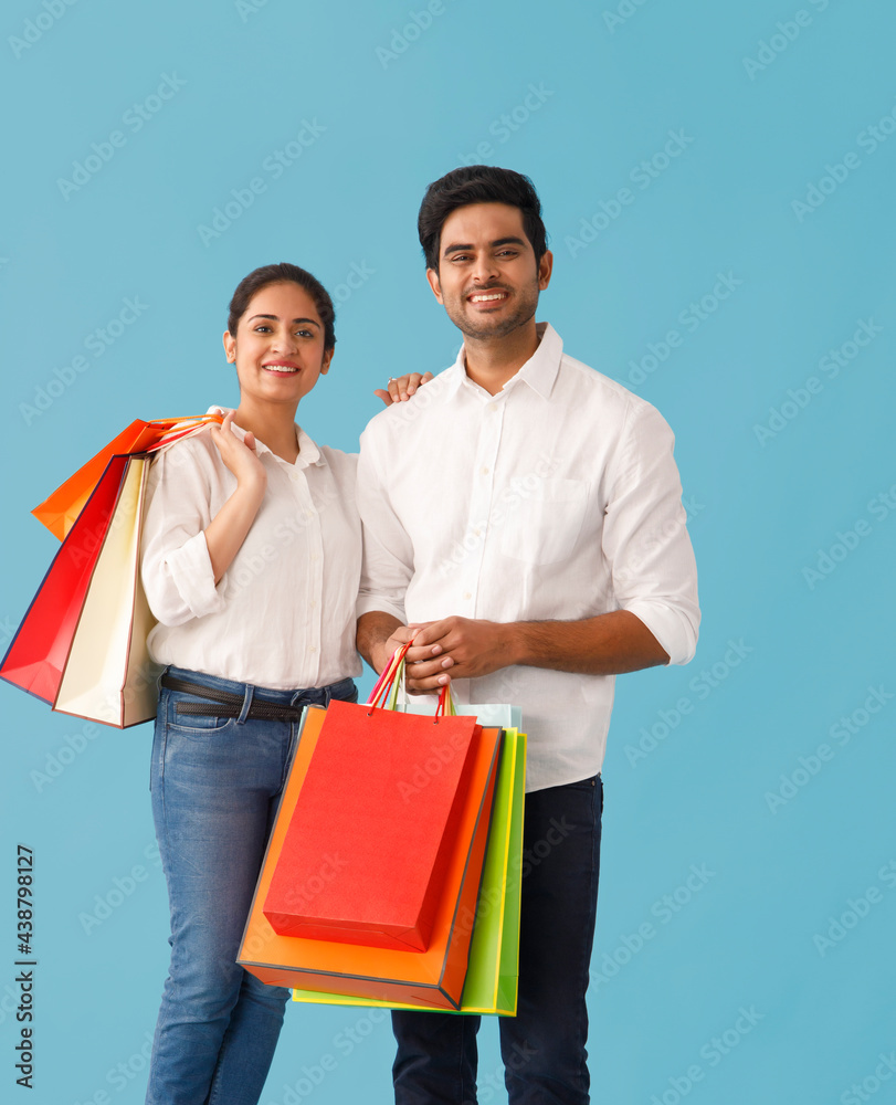 A YOUNG HAPPY COUPLE STANDING TOGETHER WHILE HOLDING SHOPPING BAGS A YOUNG HAPPY COUPLE STANDING TOGETHER WHILE HOLDING SHOPPING BAGS