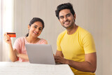 A HAPPY COUPLE SITTING AT HOME AND DOING ONLINE TRANSACTION	