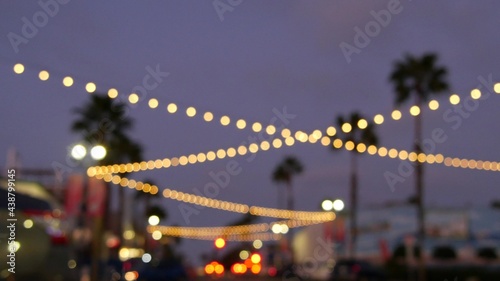 Defocused illuminated electric garland  palm trees silhouettes  Oceanside California USA. Ocean beach tropical pink sunset  pacific coast purple twilight sky. Los Angeles vibes. Bulb lights glowing.