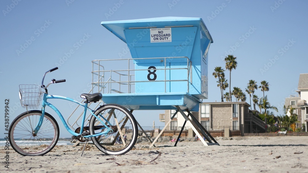 Blue bicycle, cruiser bike by ocean beach, pacific coast, Oceanside  California USA. Summertime vacations, sea shore. Vintage cycle on sand near  lifeguard tower or watchtower hut. Sky and water waves. foto de