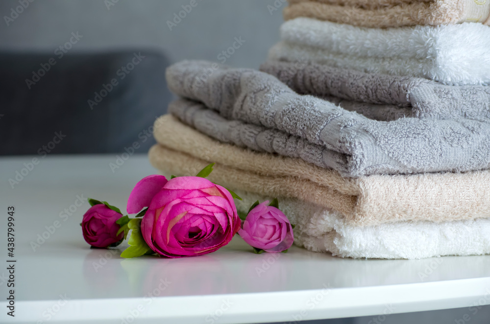 A stack of terry shower towels on a white table close-up next to artificial peony flowers A stack of terry shower towels on a white table close-up next to artificial peony flowers