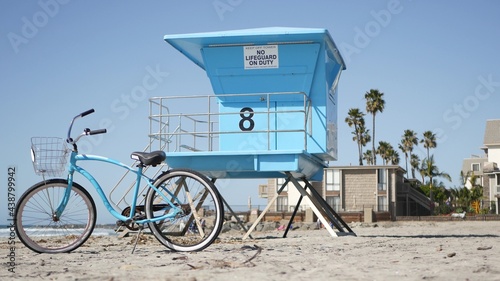 Blue bicycle, cruiser bike by ocean beach, pacific coast, Oceanside California USA. Summertime vacations, sea shore. Vintage cycle on sand near lifeguard tower or watchtower hut. Sky and water waves.