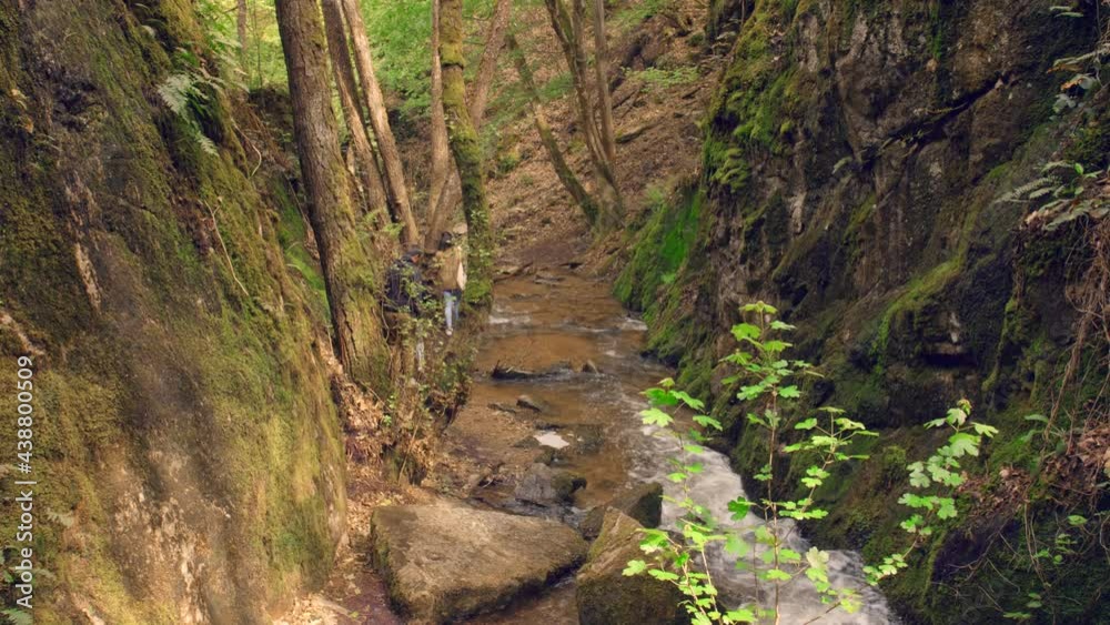 Trekkers walking along stone path near river in forest on mountain slope in sunny weather in summer. Hiker climbs down A Rocky Mountain With Narrow Path, hiking concept. Shot in 4k. Trekkers walking along stone path near river in forest on mountain slope in sunny weather in summer. Hiker climbs down A Rocky Mountain With Narrow Path, hiking concept. Shot in 4k.