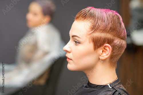 Side view portrait of a beautiful young caucasian woman with a short pink haircut waiting for a hairdresser in a beauty salon