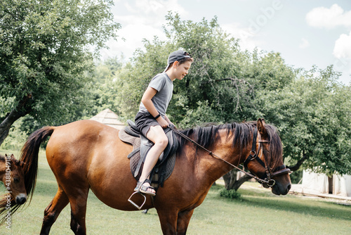Happy young boy riding a brown horse in the countryside, horse ranch in the summer