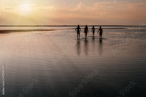 Children silhouettes walking in the water at the beach at sunset