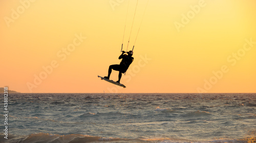 Backlit shot of a kitesurfer making a high jump in the sunset