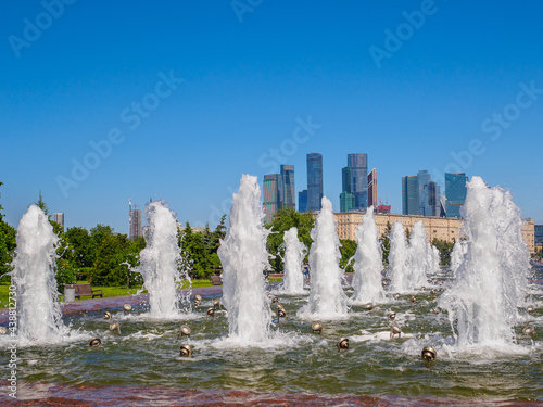Jets of fountains on a sunny day against the backdrop of modern skyscrapers and a cloudless blue sky. Recreation area in Victory Park on Poklonnaya Hill in summer.