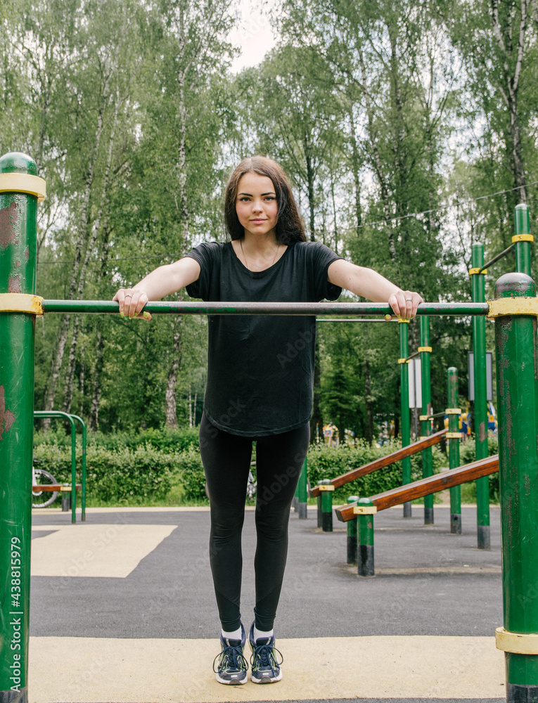 Fototapeta premium a girl in a black T-shirt and leggings shakes her hands from the horizontal bar on the playground
