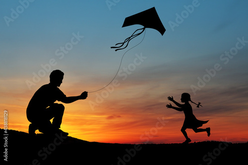 Happy family on the field. Father and daughter playing with a kite while running on meadow on the background of the sunset. Funny family time. Happy little daughter launch a kite with dad.