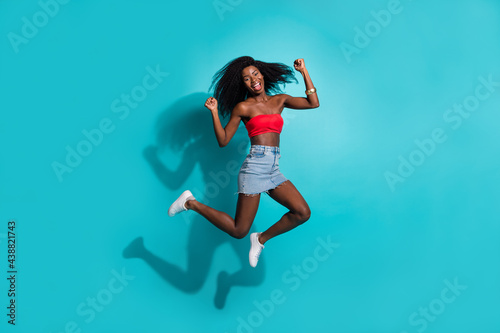 Full length body size photo woman jumping up gesturing like winner isolated on vibrant teal color background