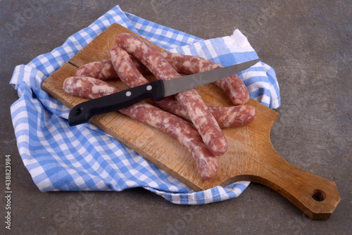 Chipolatas crues sur une planche à découper en bois avec un couteau et un torchon à carreaux en gros plan sur fond gris