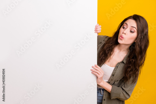 Portrait of attractive curious girl looking at white poster copy space new novelty ad pout lips isolated over vibrant yellow color background