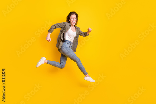 Full length photo of pretty adorable young lady wear brown shirt jumping running fast empty space isolated yellow color background