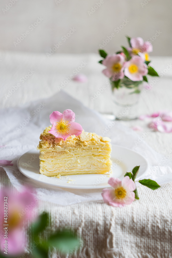 A piece of layered napoleon cake decorated with flowers on a light textile background, selective focus A piece of layered napoleon cake decorated with flowers on a light textile background, selective focus