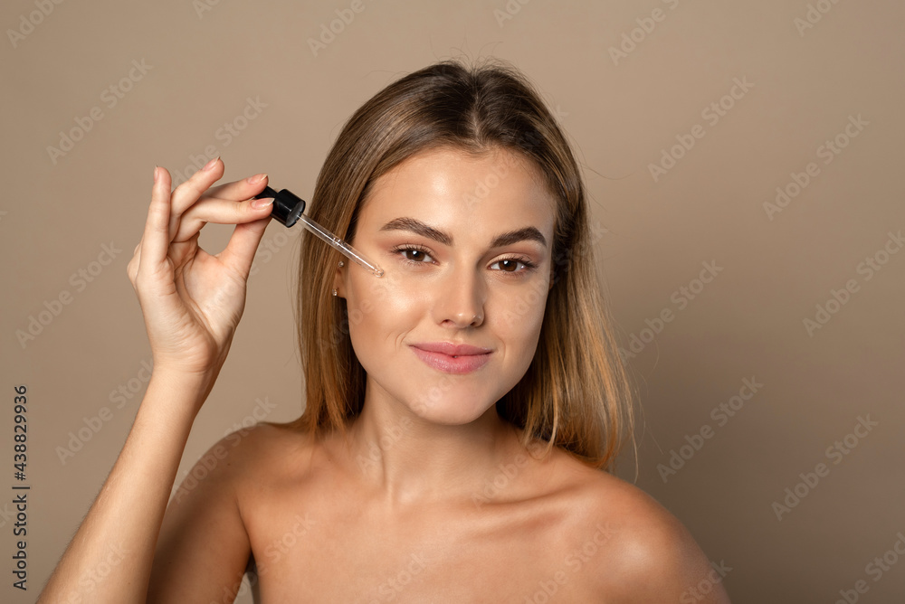 Beautiful face portrait of young woman is applying face serum on a cheek