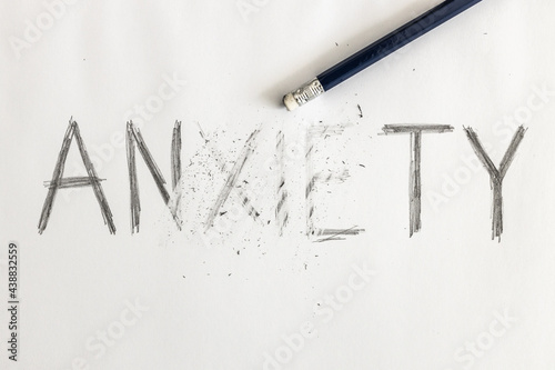 Erasing anxiety. Anxiety written on white paper with a pencil, partially erased with an eraser. Symbolic for overcoming anxiety or treating anxiety. 