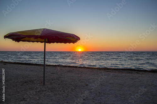 Parasol on Seaside in sunrise. Colorful sky at sunset on the horizon. Rising Sun Reflecting on Water with Calm Ocean Waves. Hope  spirituality  freedom and loneliness - concept. Morning on the beach.