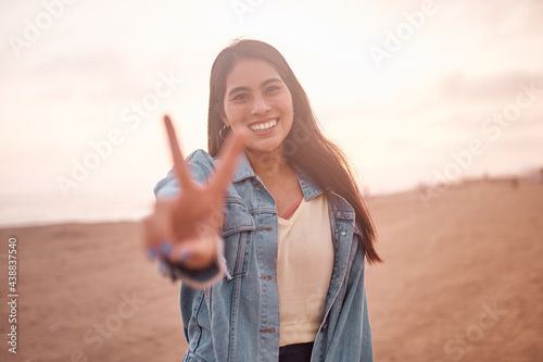 Schilderij op canvas Mujer Joven latina hace la seña de la paz sonriendo durante un bello atardecer