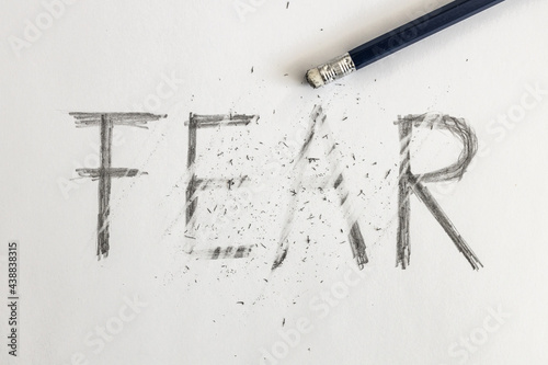 Erasing fear. Fear written on white paper with a pencil, erased with an eraser. Symbolic for overcoming fear or treating fear. photo