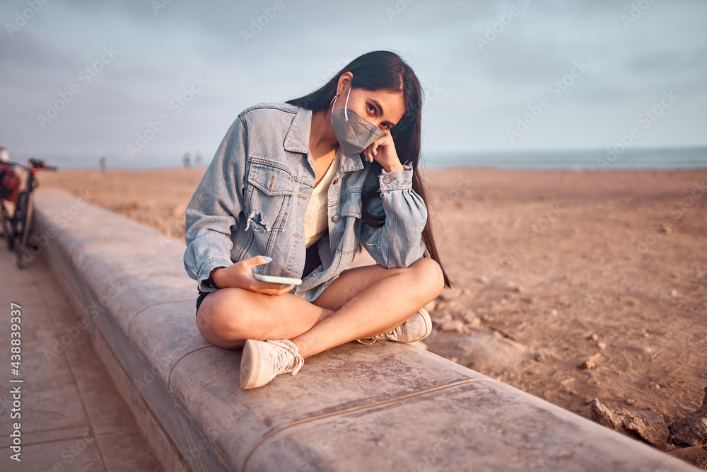 Mujer Joven latina descansando sentada durante un bello atardecer.. Joven feliz  con mascarilla en la playa