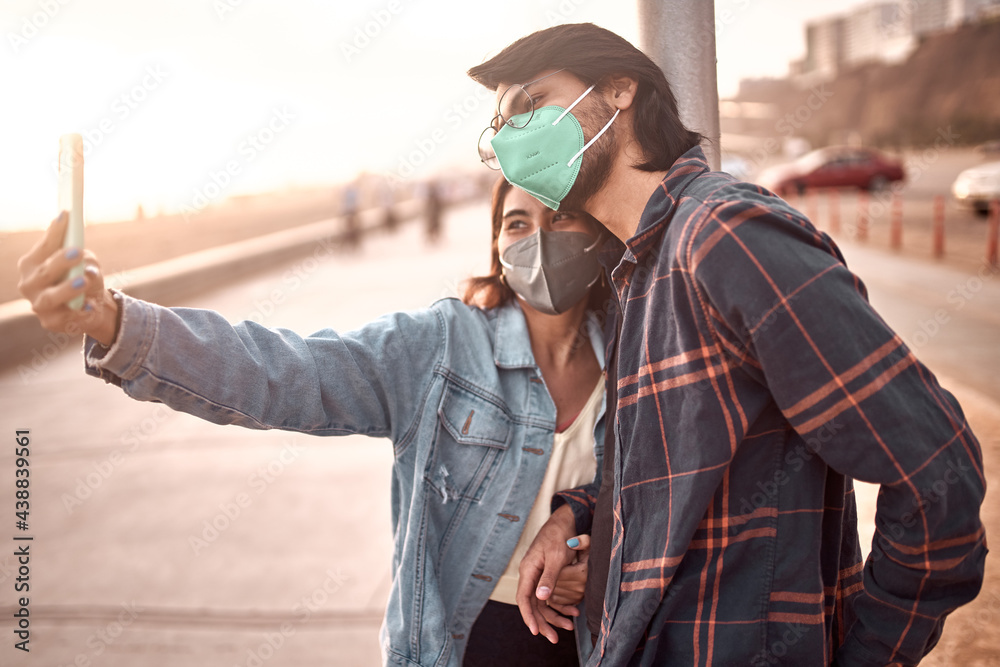 Pareja de jóvenes enamorados se toman fotografías selfies durante un bello atardecer.. Jóvenes felices jugando en malecón de la playa. Amor de pareja