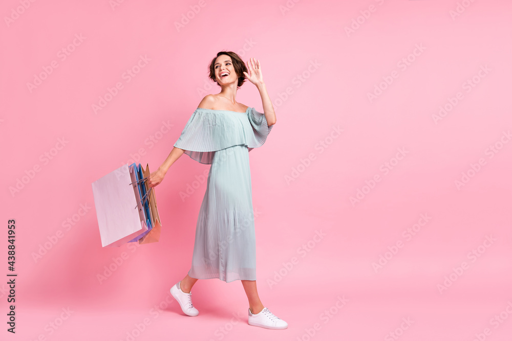 Full body profile side photo of young girl happy smile go walk wave hello hold shopping bags isolated over pastel color background Full body profile side photo of young girl happy smile go walk wave hello hold shopping bags isolated over pastel color background