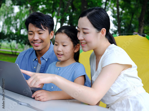 Happy family of three use computer to surf the Internet outdoors