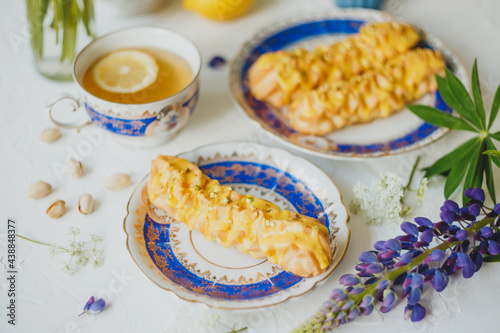 Lemon eclairs and lemon tea  in a vintage tea set  and flowers  over white background.