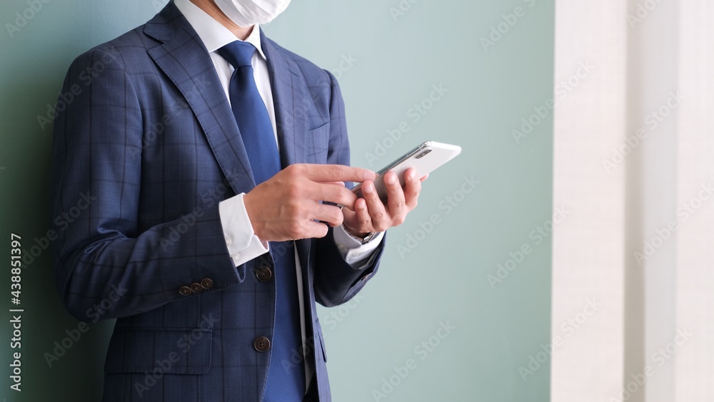 スマホを操作しているマスクをしたサラリーマン男性 スマホを操作しているマスクをしたサラリーマン男性