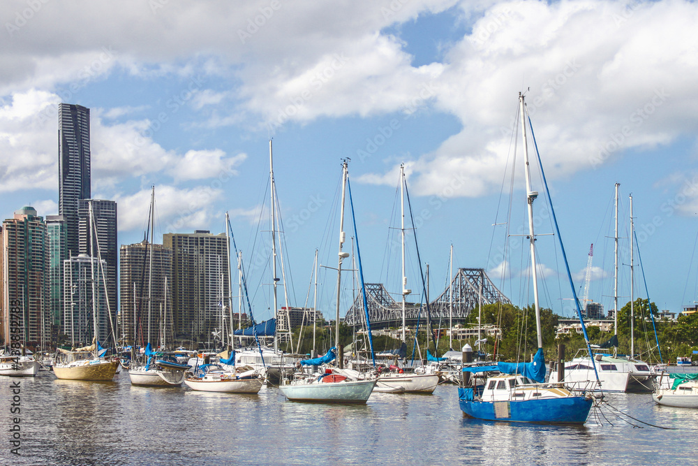 Sailboats moored in the Brisbane River with towers of CBD and Story Bridge in the ackground