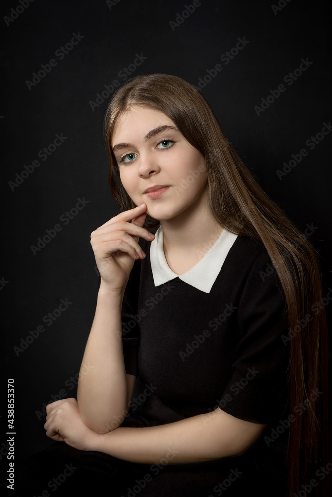Portrait of a beautiful young girl with straight long hair and blue eyes, in black clothes on a black background, waist-deep, with a hand touching her face Portrait of a beautiful young girl with straight long hair and blue eyes, in black clothes on a black background, waist-deep, with a hand touching her face