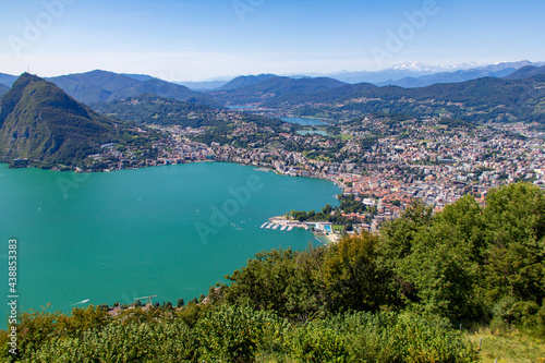 View from hills in near Lugano city over Lugano lake during summer in Switzerland. Turqoise water and snowy alps mountains.